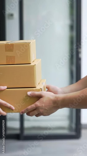 A tight medium close-up video focuses on a professional delivery person's clean hands, in a modern uniform, smoothly handing unbranded brown boxes to a recipient's eager hands, blurred modern
