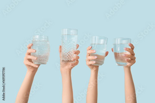 Female hands with glasses of cold water on blue background