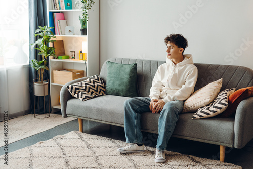 Obraz na plátně Young man sitting on sofa looking pensive in modern living room