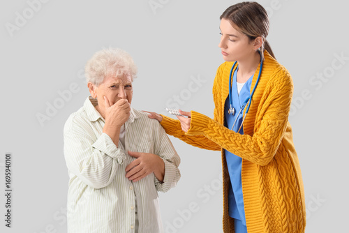 Nurse giving pills to ill senior woman on light background