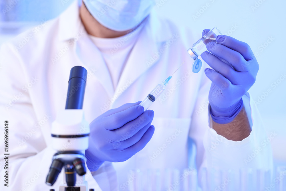 Fototapeta premium Male scientist with ampoule and syringe in laboratory, closeup