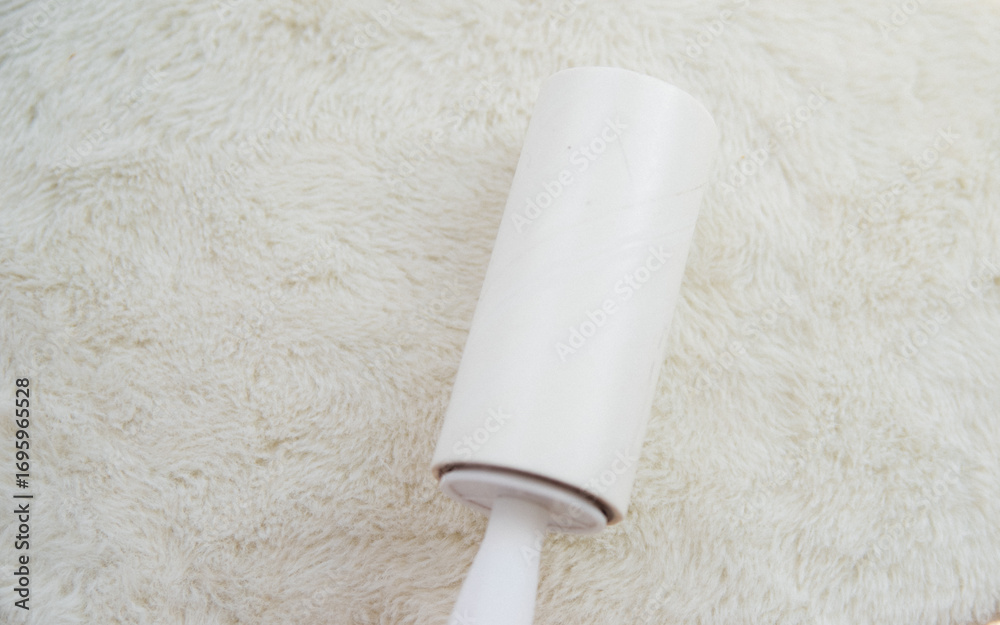 Obraz premium A woman's hand cleans the white soft surface of the furniture with a sticky roller. Cleaning of upholstered furniture from dust, wool and hair.