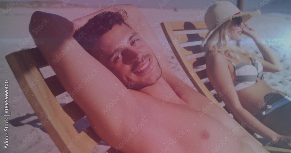 Fototapeta premium Couple reclining on beach loungers at sand dunes, wearing swimwear and straw sun hat