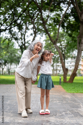 Wallpaper Mural Old woman grandmother holding hand and pointing away with kid girl granddaughter on park's pavement. Torontodigital.ca