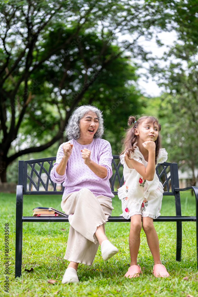Fototapeta premium Old woman granny shaking arms cheering for a kid girl granddaughter dancing on grass in the park.