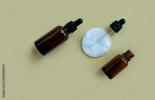 Flat lay vials with a pipette and a white cotton pad on a beige background.