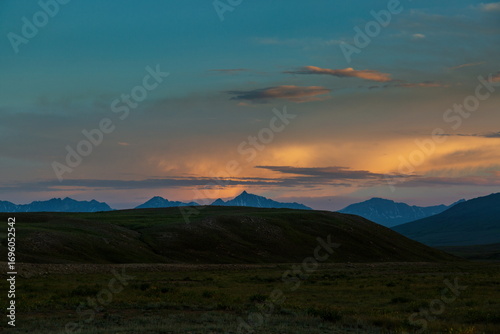 View of golden light paints the distant peaks as shadows lengthen across the rolling green hills, a serene landscape at dusk, Skardu, Gilgit Baltistan, Pakistan.