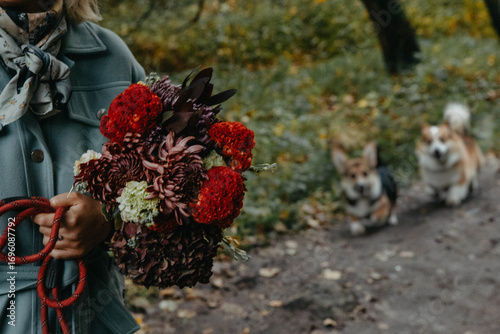 A woman holds a bouquet of flowers with two dogs behind her
