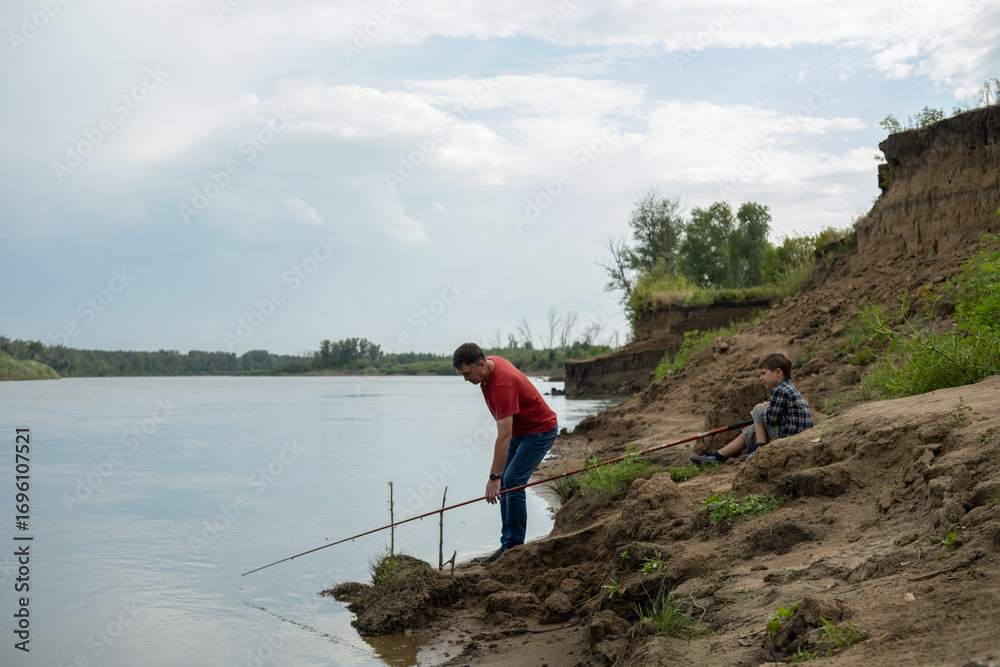 Fototapeta premium Grandfather is teaching a grandson fishing on the river beach.