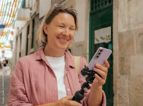 Vlogger traveler woman recording video on phone share via app travel vacation. Middle age woman influencer shooting social media stories on decorated street of Alfama district in Lisbon, Portugal. UGC