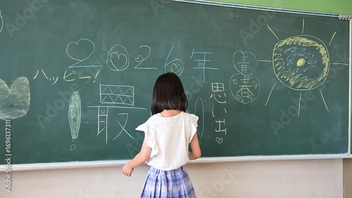教室の黒板に文字を書く小学生の女の子