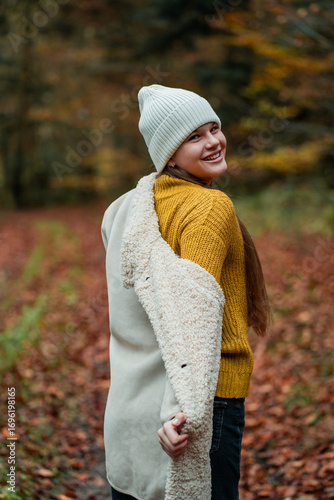 Portrait of a happy teenage girl in a hat and warm clothes on a walk in the autumn forest. Meditation and relaxation in nature.