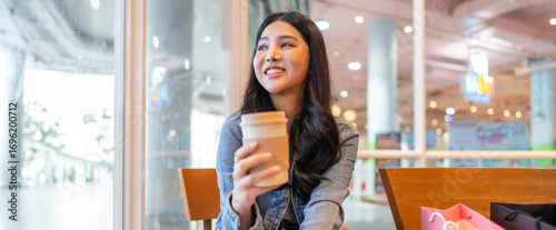 Asian freelance woman enjoying premium coffee drink in cozy cafe, casual workday lifestyle, delivery coffee, cafe trend, relaxing after shopping, modern urban working culture for young professionals