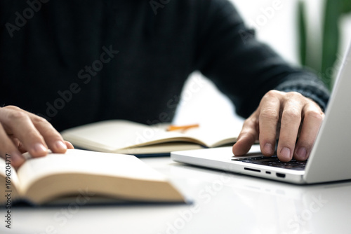 Closeup image of a male writing notes in his notebook while using laptop. Boy working on new project