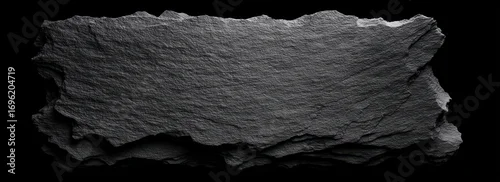 Panel kuchenny z motywem A stacked slate slab. Rough, textured surface on layered rock fragments. Dark gray material isolated against a black background creates contrast