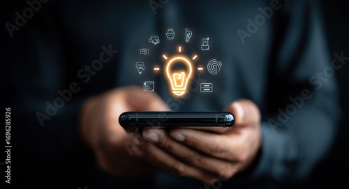 Person holding smartphone, glowing bulb above, with tiny icons. Dark, blurred background adds focus