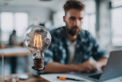 Blurred man with a beard works on a laptop, lightbulb floats next to him in office space