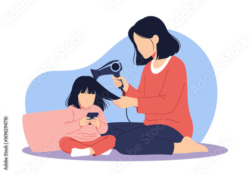 Mother drying daughter's hair while she plays on her phone relaxing family time together