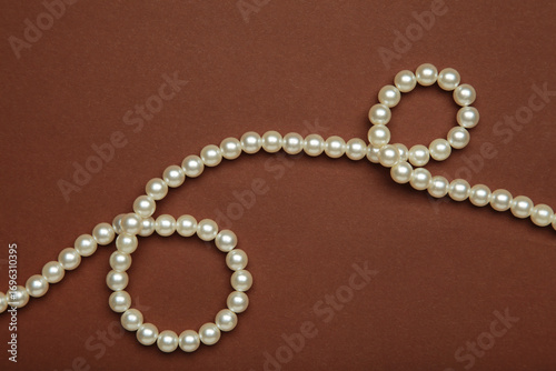 Elegant pearl necklace on dark brown background, top view.