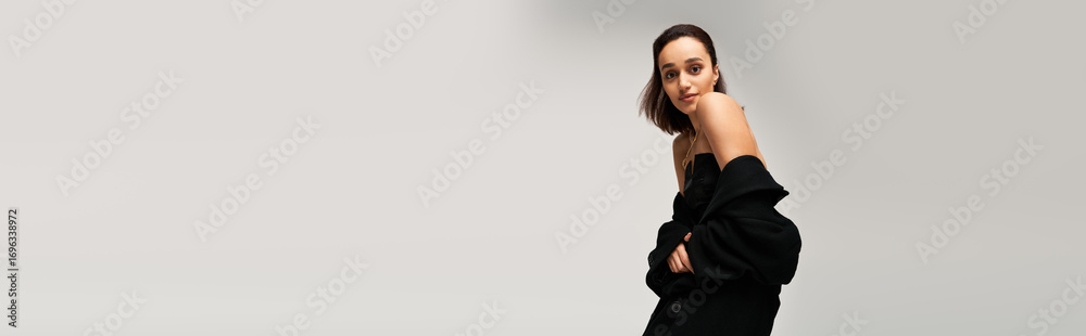 Fototapeta premium Brunette woman exudes modern elegance in a black outfit in a studio