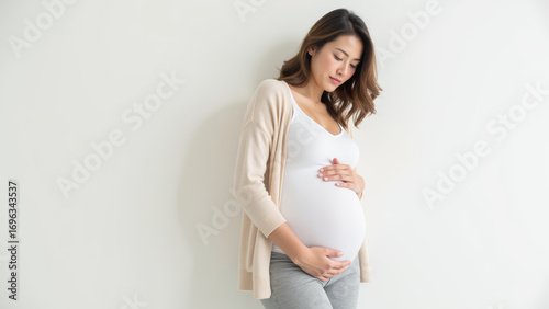 Serene pregnant woman gently cradles her baby bump, showcasing beauty of motherhood against light background Free Download Serene pregnant woman gently cradles her baby bump, showcasing beauty of motherhood against light background - GFXLoad