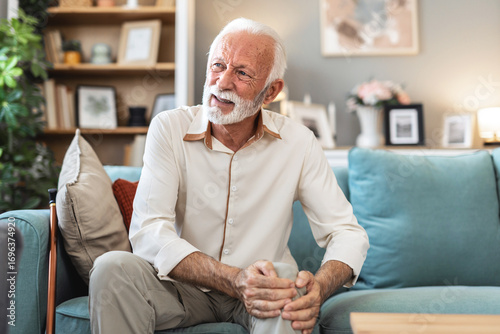 Hands, knee pain and senior person on sofa in living room of apartment with arthritis or osteoporosis. Inflammation, injury or joint problem with old man in retirement home closeup with fibromyalgia.