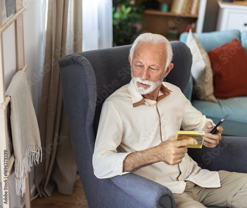 Phone, pills and senior man at home, reading label, medicine information and confused for telehealth service or FAQ. Elderly person on sofa with pharmaceutical bottle or tablet with mobile questions.