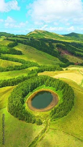 Pond Pau Pique and Lush Green Hills with Pasturelands and Trees. Moving Shadows from Clouds. Azores, Sao Miguel Island. Portugal. Aerial View. Orbiting. Vertical Video