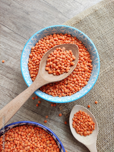 Dried small red lentils in a decorative plate and wooden spoons on a wooden background