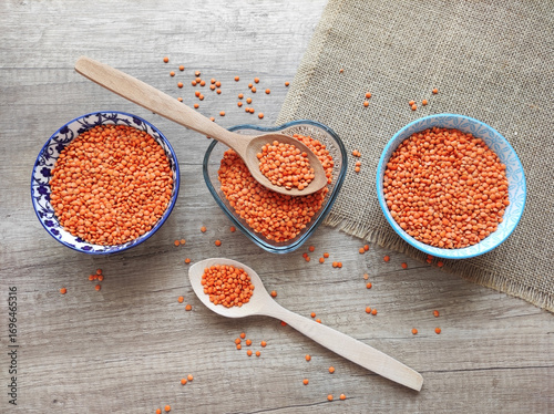 Dried small red lentils in a decorative plate and wooden spoons on a wooden background