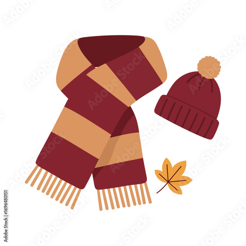 A cozy knitted maroon and tan striped scarf and a matching beanie hat with a pom-pom, accompanied by a fallen autumn leaf.
