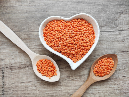 Dried small red lentils in a decorative plate and wooden spoons on a wooden background