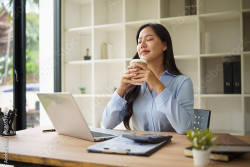 Businesswoman enjoying coffee break while working at modern office desk.