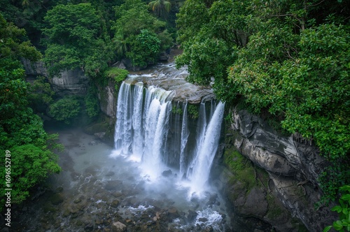 Aerial perspective of a tropical waterfall surrounded by lush greenery and ocean views