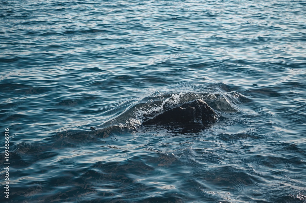 Naklejka premium Soft ocean waves create intricate designs as they crash onto an isolated stone, shimmering in the bright sunlight and reflecting the sea's tempo.