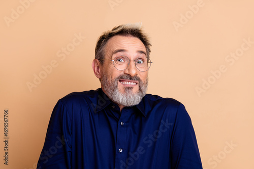 Fotografie Mature man in blue shirt showing a quirky expression against a beige backdrop, r