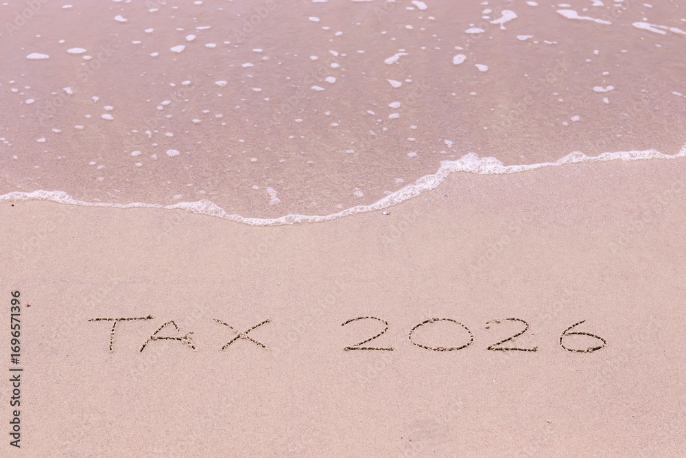 Fototapeta premium TAX 2026 handwritten with ocean waves on a sandy beach.