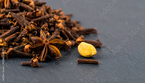Fototapeta Naklejka Na Ścianę i Meble -  Close-up shot of a pile of brown cloves with a single star anise and cardamom pod on a dark surface.