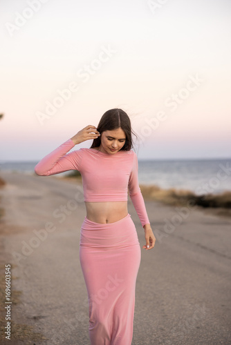 An Elegant Woman Dressed in a Beautiful Pink Dress Standing by the Beach at Stunning Sunset