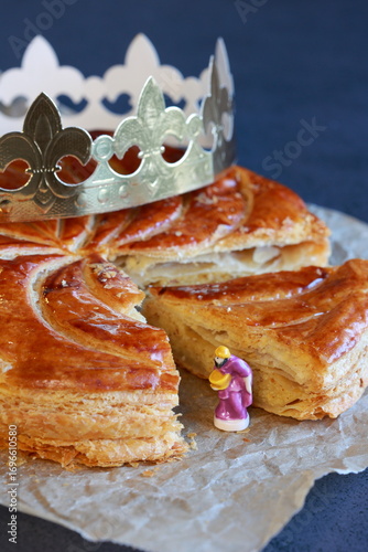 Galette des rois with a golden crown and figurine of king stands out on dark vertical background 