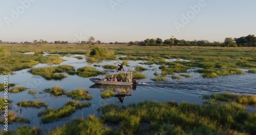 Aerial panning. Tourists on a sightseeing boat on a river in the Okavango Delta at sunset