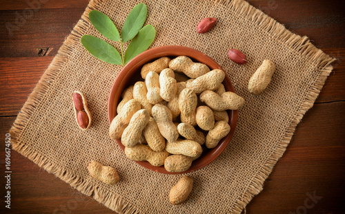 Handful of peanuts in container on sackcloth mat on wooden