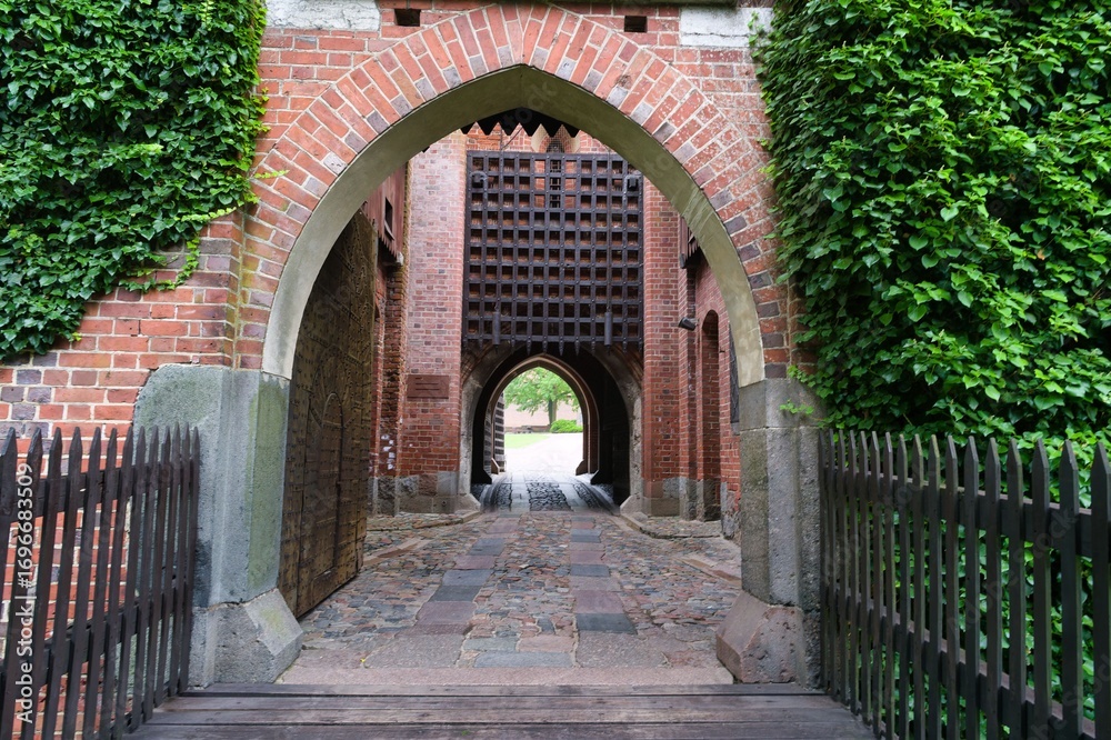 Fototapeta premium Beautiful historic brick archway leading to a serene courtyard in a medieval castle during a sunny day