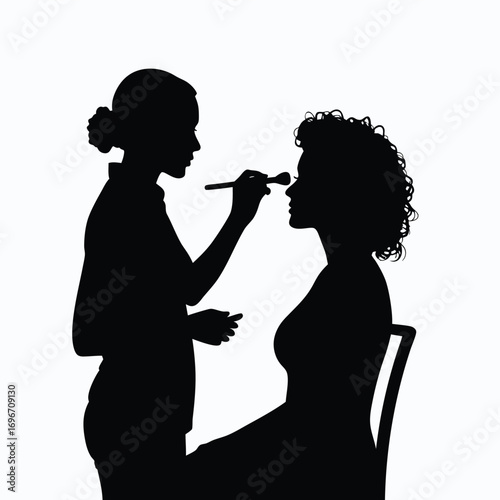 Silhouette of makeup artist applying makeup to woman in chair