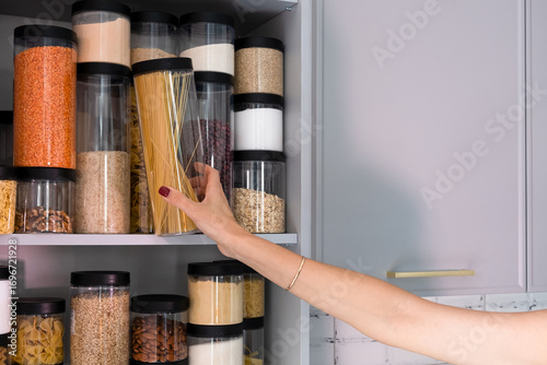 Organized kitchen pantry with cylindrical plastic jar for storing loose products,  in grey tones