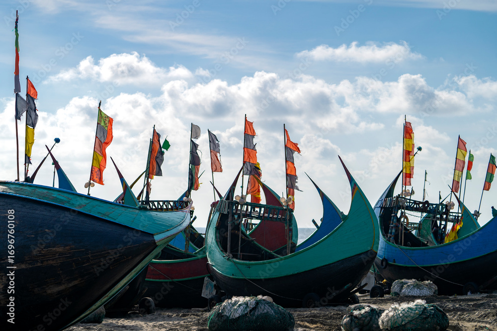 Obraz premium Fishing boats at the beach with colorful flags under a cloudy sky. Colorful Wooden Fishing Boat On a Cox's Bazar Sea Beach, Bangladesh With Blue Sky Background.