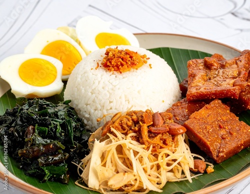 Indonesian Nasi Uduk, Indonesia Savory Rice with Many Topping such as Cucumber, Side Dish, Egg, Tempeh, Vegetables, and Sambel in the Banana Leaf Plate with Smooth Background