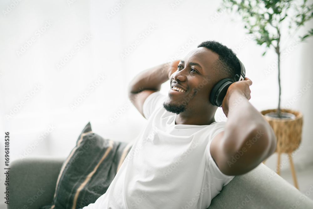 Fototapeta premium Cheerful black man using headphone on sofa.