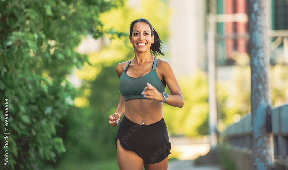 Fototapeta premium Happy sporty woman jogging outdoors in urban scene
