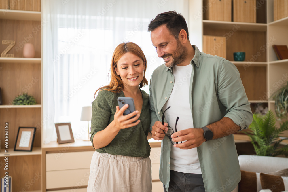 Obraz premium Couple smiling and using smart phone at home